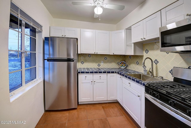 kitchen with ceiling fan, tile countertops, appliances with stainless steel finishes, white cabinetry, and a sink