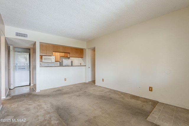 unfurnished living room featuring stacked washer and dryer, light colored carpet, visible vents, and a textured ceiling