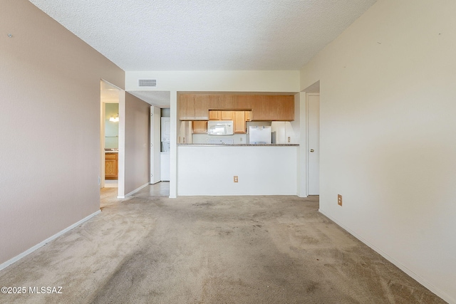 unfurnished living room featuring light colored carpet, visible vents, a textured ceiling, and baseboards