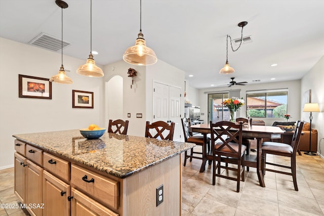 kitchen featuring arched walkways, light stone counters, visible vents, and a center island