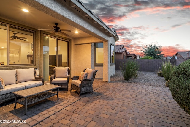 patio terrace at dusk with outdoor lounge area, fence, and a ceiling fan