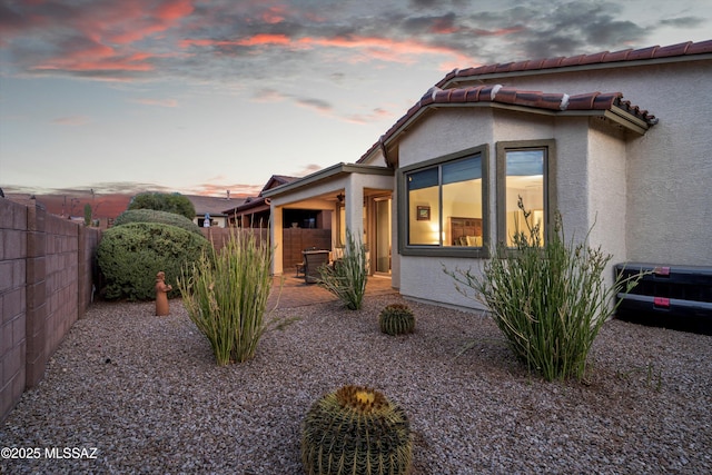 view of side of property featuring ceiling fan, a fenced backyard, a tiled roof, stucco siding, and a patio area