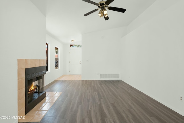 unfurnished living room with a tile fireplace, wood finished floors, a ceiling fan, visible vents, and baseboards