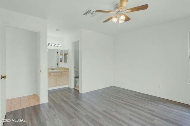 unfurnished bedroom with visible vents, ensuite bathroom, a ceiling fan, a sink, and wood finished floors