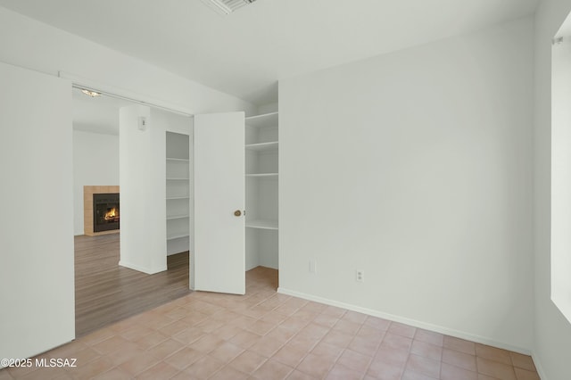 unfurnished bedroom featuring a walk in closet, a closet, a fireplace, and baseboards