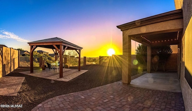 patio terrace at dusk with a fenced backyard, a gazebo, and a pergola