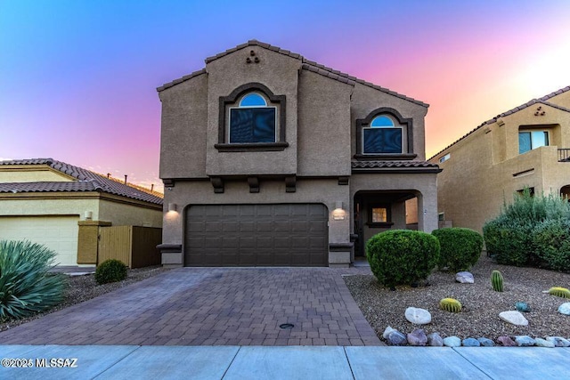 mediterranean / spanish home featuring a garage, a tiled roof, decorative driveway, and stucco siding