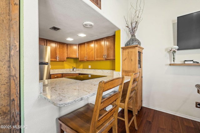 kitchen with visible vents, light stone counters, freestanding refrigerator, baseboards, and dark wood-style flooring