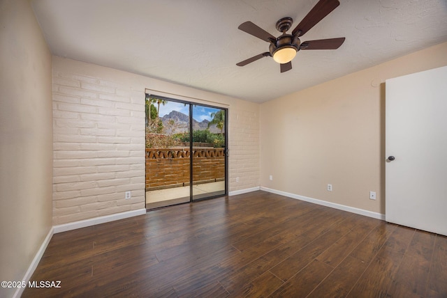 unfurnished room with brick wall, wood finished floors, and baseboards