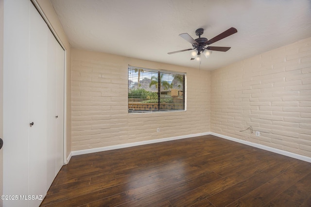 unfurnished room featuring brick wall, baseboards, and dark wood finished floors