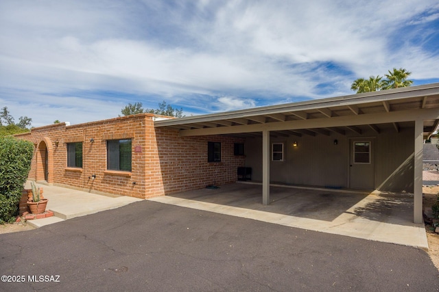 rear view of house with aphalt driveway, an attached carport, and brick siding