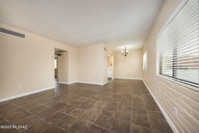 spare room featuring baseboards, visible vents, brick wall, and an inviting chandelier