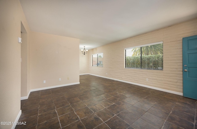 unfurnished room featuring brick wall, a chandelier, and baseboards