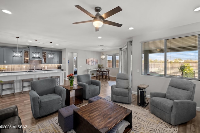 living area featuring ceiling fan with notable chandelier, recessed lighting, wood finished floors, and baseboards