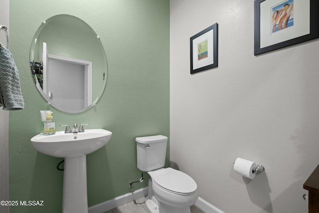 half bath featuring baseboards, a sink, and toilet