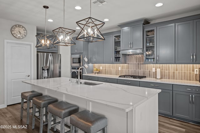 kitchen featuring under cabinet range hood, appliances with stainless steel finishes, decorative backsplash, and a sink