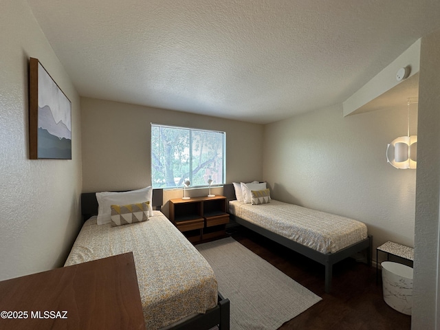 bedroom featuring a textured ceiling, a textured wall, and wood finished floors