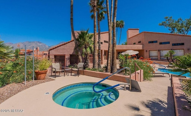 pool with a patio area, fence, a mountain view, and a hot tub