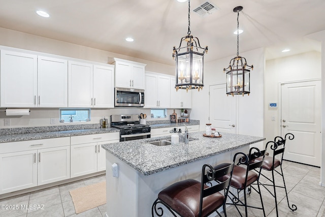 kitchen featuring visible vents, a breakfast bar area, stainless steel appliances, white cabinetry, and a sink