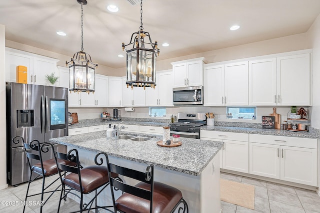 kitchen with pendant lighting, stainless steel appliances, white cabinets, a sink, and an island with sink