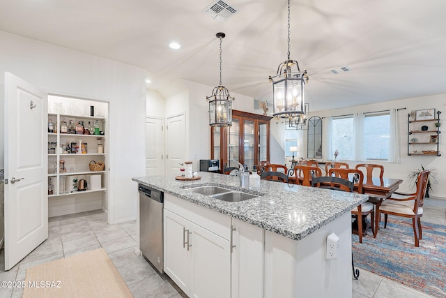 kitchen with light stone counters, a sink, visible vents, stainless steel dishwasher, and a center island with sink