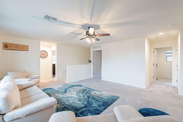 living area with attic access, visible vents, light carpet, and a ceiling fan