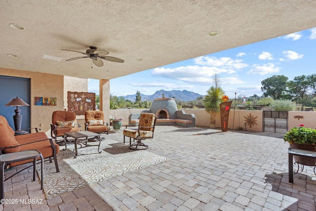 view of patio / terrace featuring an outdoor living space with a fireplace, a ceiling fan, a gate, fence, and a mountain view