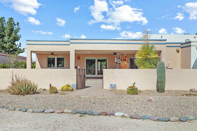 pueblo-style home featuring a fenced front yard, stucco siding, and a ceiling fan