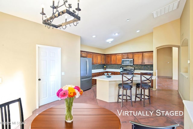 kitchen with light tile patterned floors, visible vents, arched walkways, stainless steel appliances, and backsplash