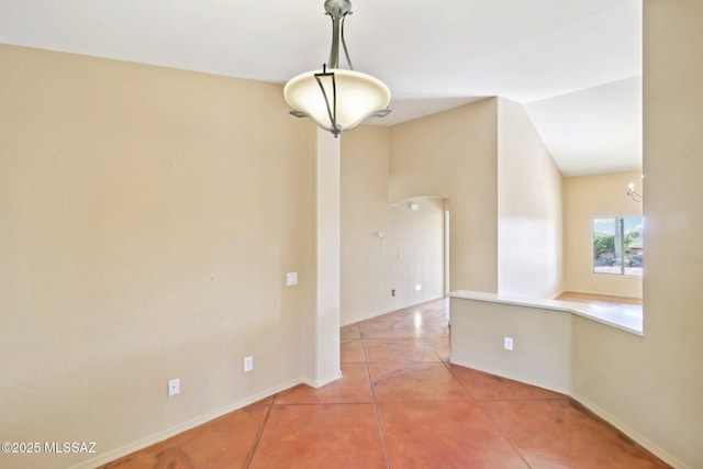 tiled spare room featuring baseboards and vaulted ceiling