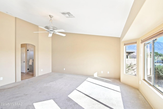 empty room featuring lofted ceiling, carpet flooring, visible vents, and arched walkways