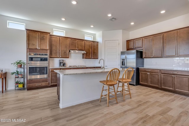 kitchen with visible vents, under cabinet range hood, a center island with sink, a breakfast bar, and appliances with stainless steel finishes