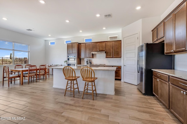 kitchen with a breakfast bar, decorative backsplash, a center island with sink, and stainless steel appliances