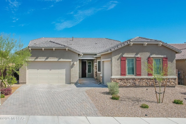 ranch-style home featuring decorative driveway, a tiled roof, an attached garage, and stucco siding