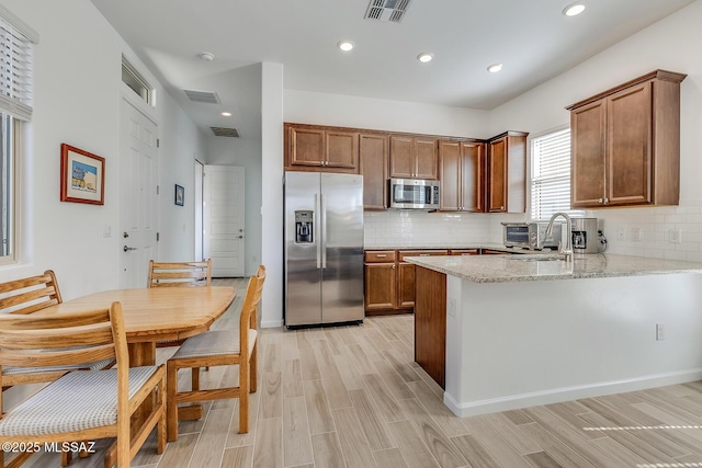 kitchen featuring visible vents, brown cabinets, a sink, appliances with stainless steel finishes, and a peninsula