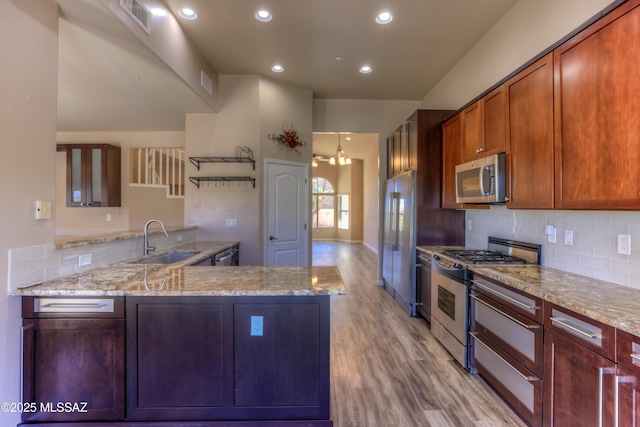 kitchen with a sink, stainless steel appliances, light stone counters, and light wood-type flooring