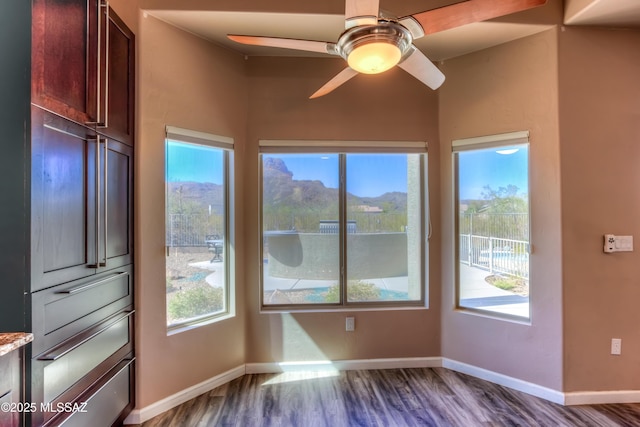 interior space with a mountain view, baseboards, dark wood-type flooring, and ceiling fan