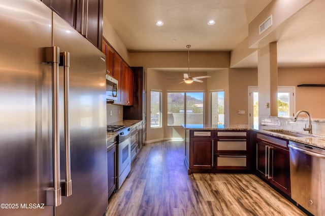 kitchen featuring visible vents, dark wood-type flooring, light stone counters, stainless steel appliances, and a sink