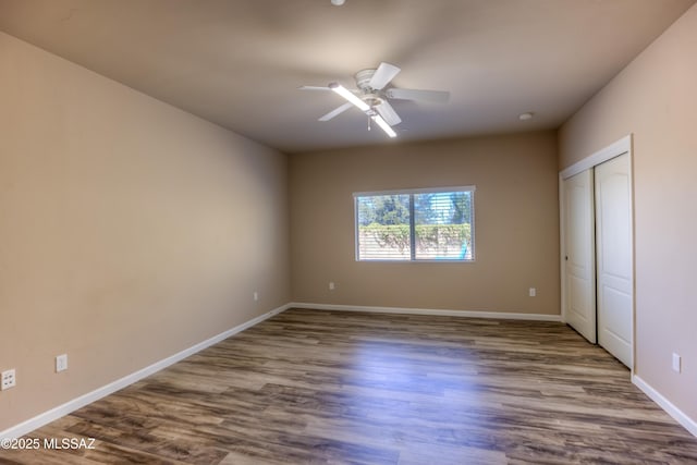 unfurnished bedroom featuring a closet, baseboards, dark wood-style floors, and a ceiling fan