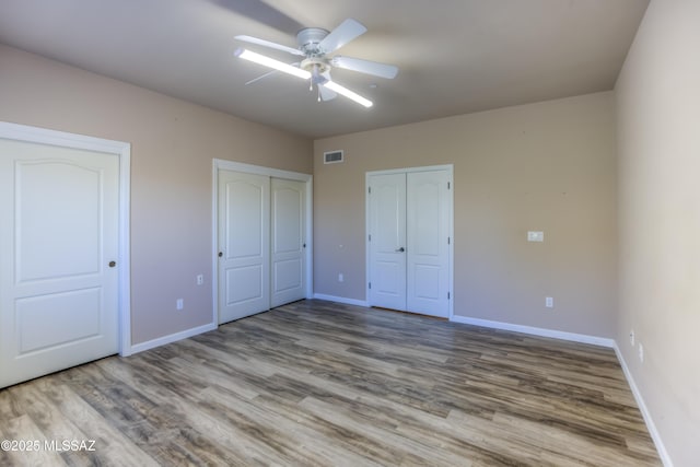 unfurnished bedroom with visible vents, two closets, baseboards, wood finished floors, and a ceiling fan