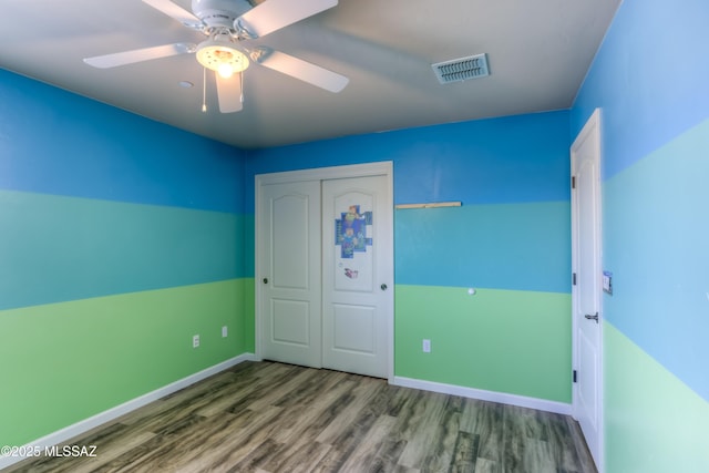 unfurnished bedroom featuring a ceiling fan, wood finished floors, visible vents, baseboards, and a closet