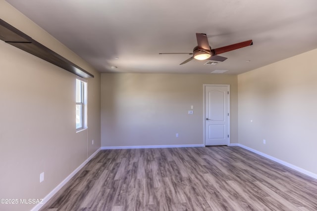 empty room with wood finished floors, a ceiling fan, visible vents, and baseboards