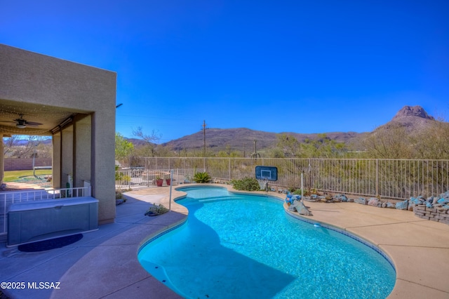 view of swimming pool featuring a fenced in pool, ceiling fan, fence, a patio area, and a mountain view