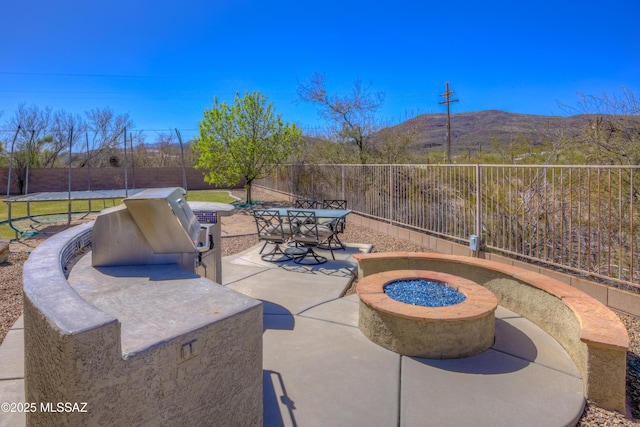 view of patio featuring outdoor dining space, a mountain view, a fire pit, and a fenced backyard