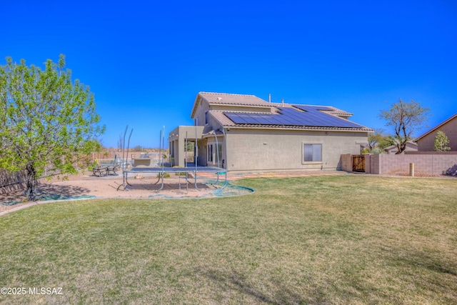 back of property featuring stucco siding, solar panels, a lawn, and a trampoline