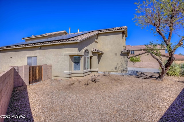 rear view of property with a tiled roof, stucco siding, solar panels, and fence