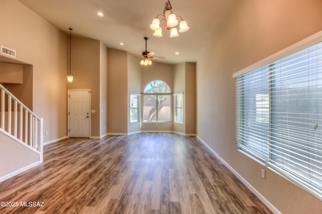 unfurnished living room featuring wood finished floors, ceiling fan with notable chandelier, baseboards, and visible vents