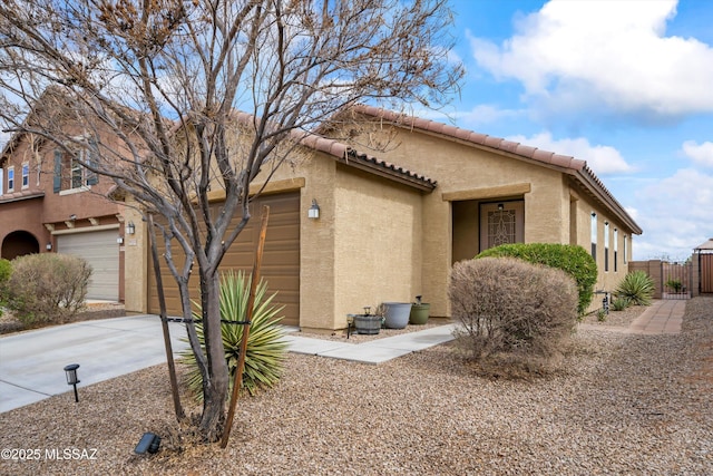 view of front of property with fence, driveway, an attached garage, stucco siding, and a tile roof