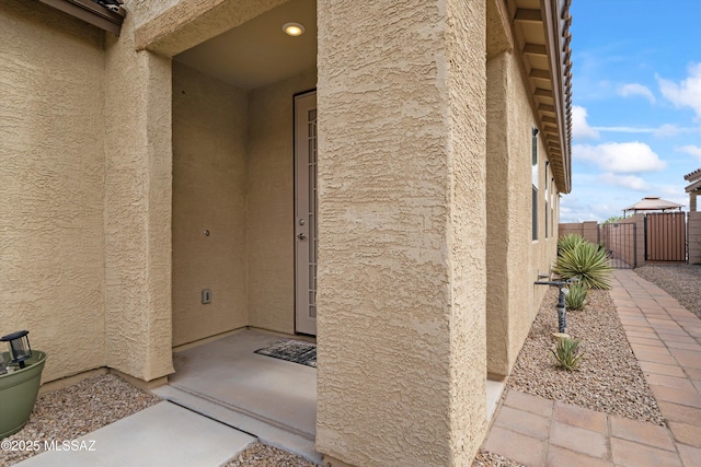 doorway to property featuring a gate, stucco siding, and fence