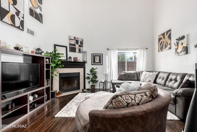 living room featuring a high end fireplace, visible vents, dark wood-style flooring, and a towering ceiling